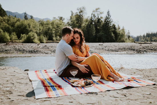 a woman in a yellow dress and a man snuggle on a picnic blanket next to a sandy stream during their Olympic National Park Adventure Elopement