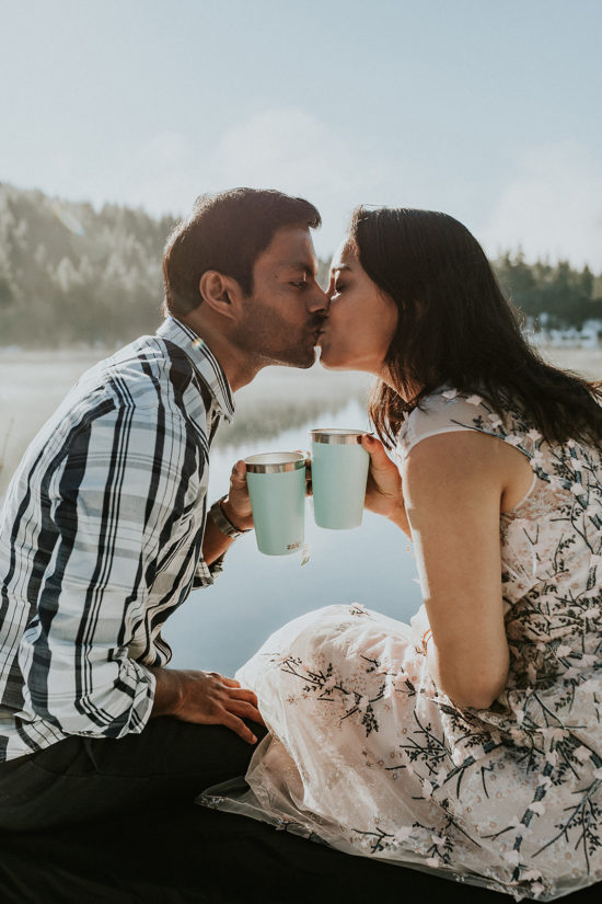 a bride and groom share a kiss and tea in mint-colored mugs in front of a misty lake during sunrise during their Snoqualmie, Washington Adventure Elopement