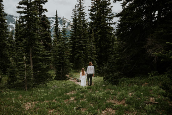 a bride and groom stand side by side holding hands among alpine firs during their Mt. Rainie Washington Adventure Elopement