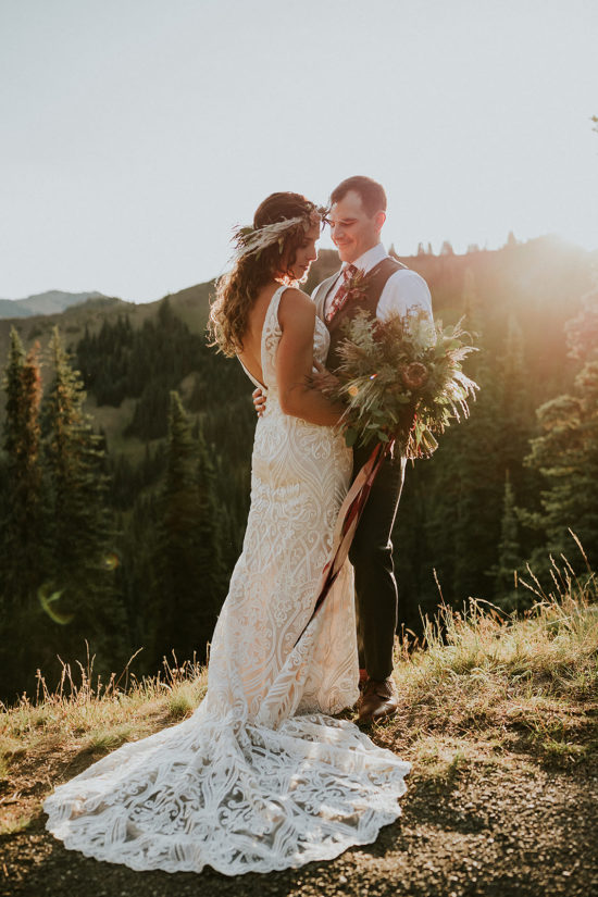 a bride holding a bouquet in a boho dress and a groom in a suit vest embrace in golden light on hurricane ridge during their Olympic National Park Washington Adventure Elopement
