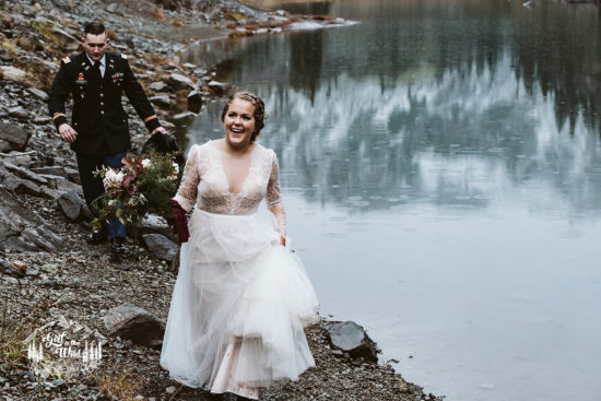 a bride in a tulle dress and hiking boots is followed by the groom in a military uniform next to a mountain lake during their North Cascades Washington Adventure Elopement